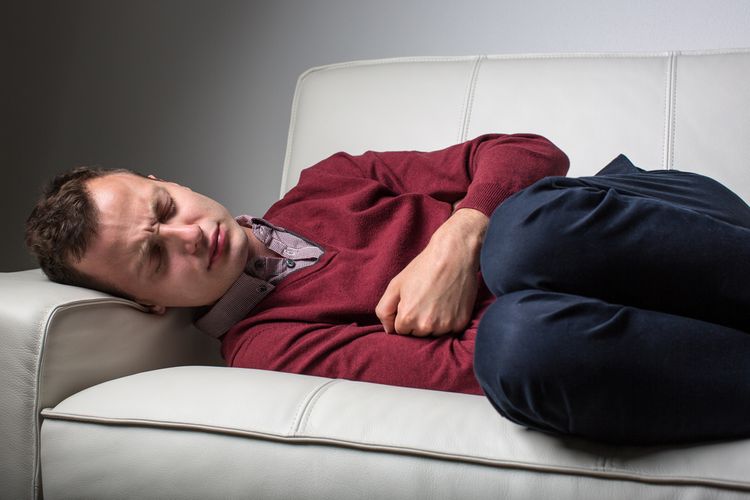 Muž trpící Crohnovou chorobou leží v bolestech na gauči