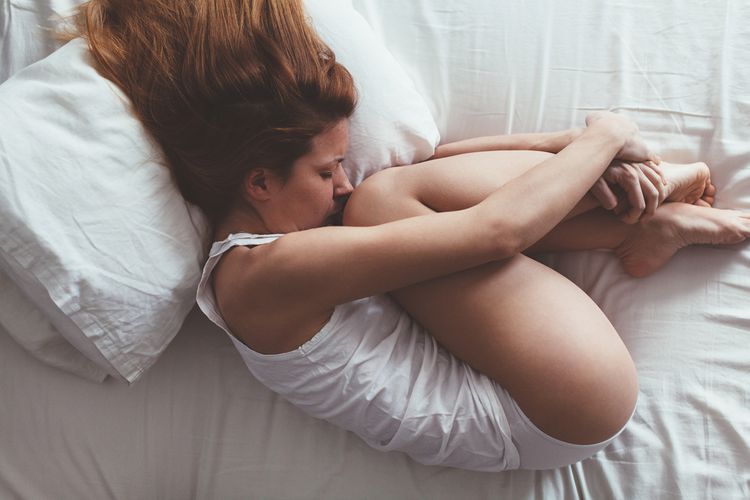 Žena s PMS – ležící v klubíčku na posteli