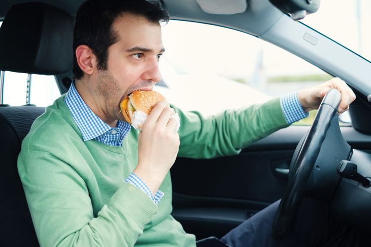 Nezdravé stravovací návyky - muž konzumující hamburger v autě