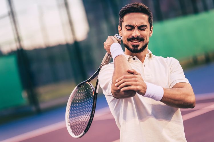 Muž s bolestí lokte během hraní tenisu